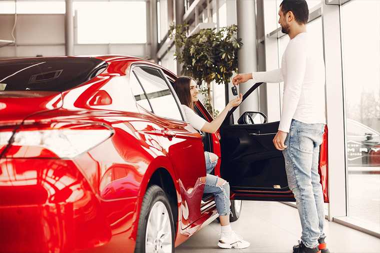 A women getting off from a red car and hand car key to a man standing beside the car